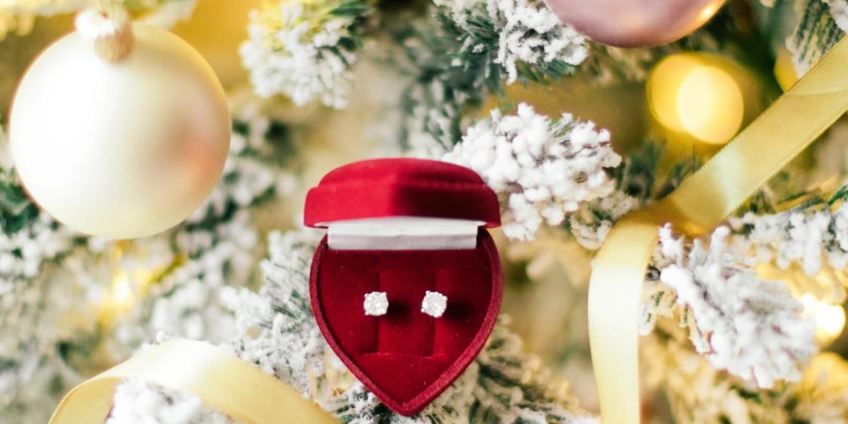 Red velvet jewelry box with diamond earrings on a snow-covered Christmas tree with golden ribbons.