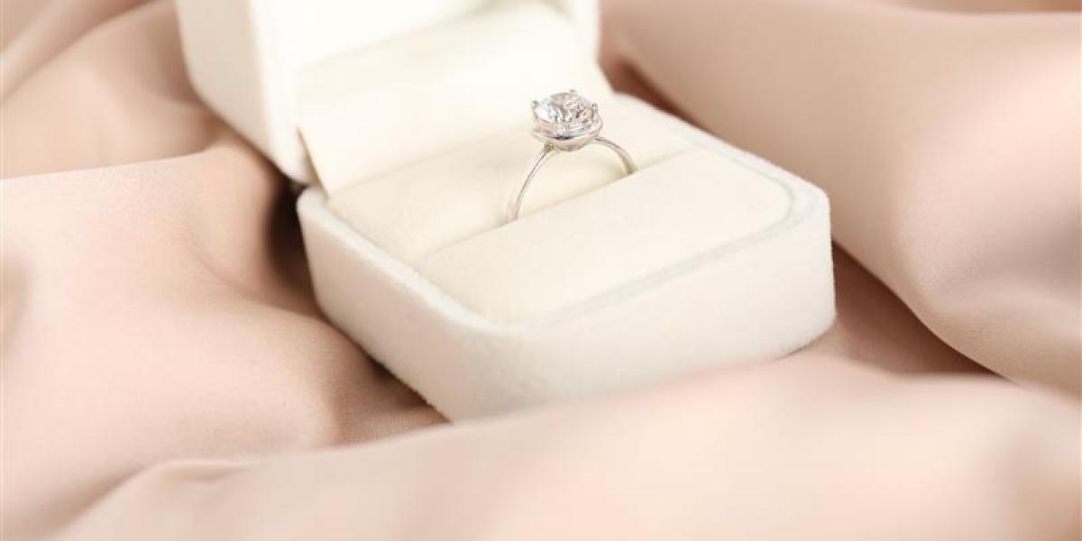 Elegant diamond engagement ring in a white velvet box placed on soft blush-colored satin fabric.