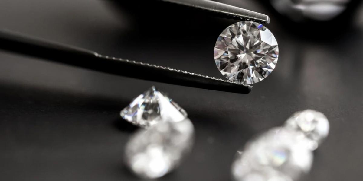 Close-up of diamonds on dark background with one diamond being held between tweezers